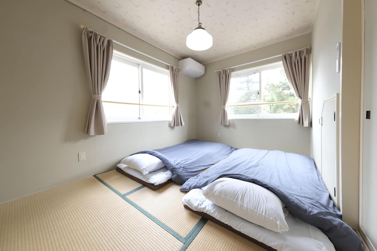 A room with two beds, a ceiling fan, and windows with curtains.