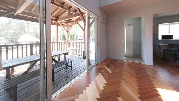 A spacious indoor area with a wooden floor, a glass door leading to an outdoor deck, and a visible kitchen area. - Shakunagedaira Vacation Rental Lot 1 (Inawashiro)