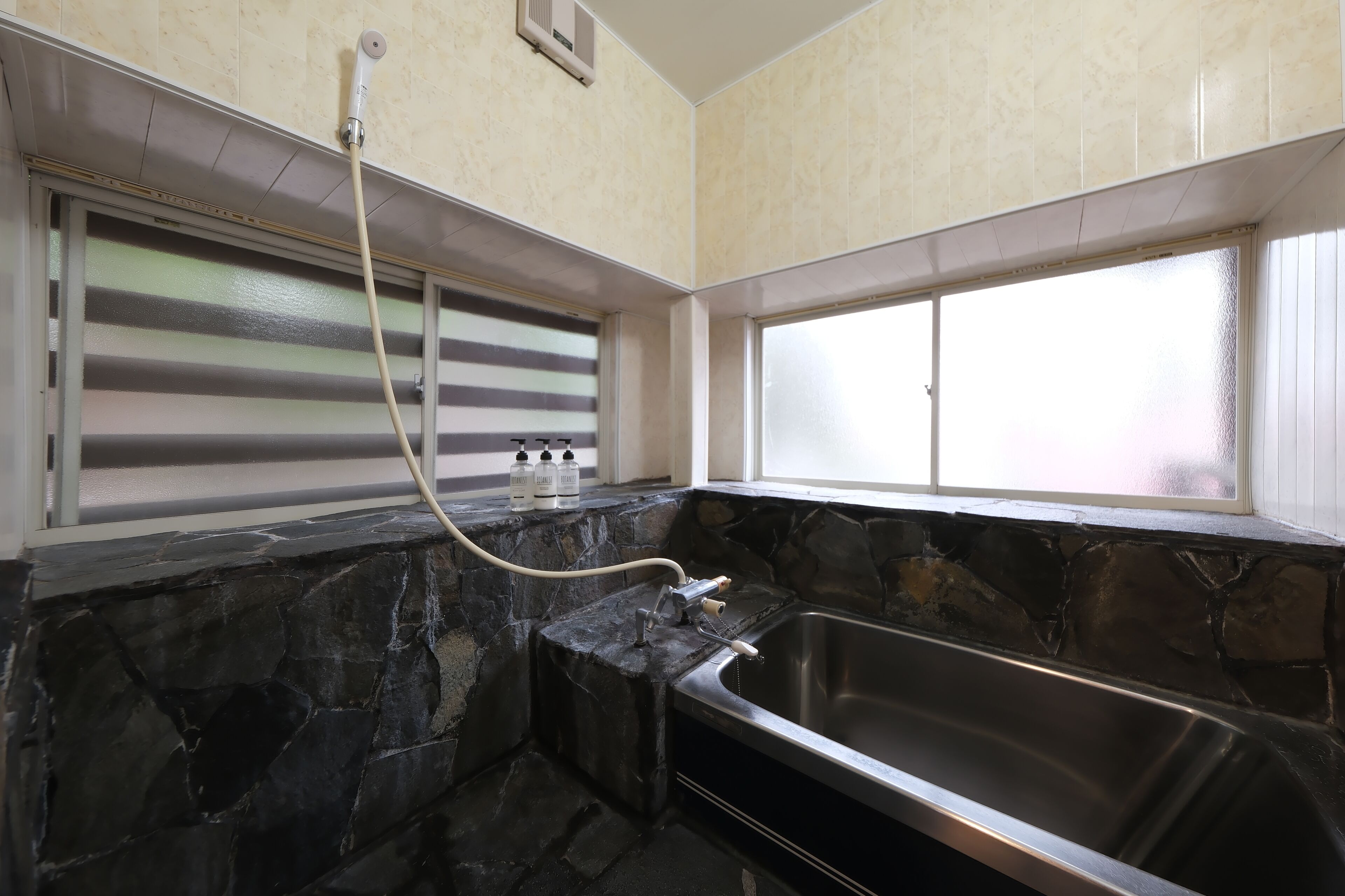 Une salle de bain avec un mur en pierre, une fenêtre, une baignoire et un flexible de douche.