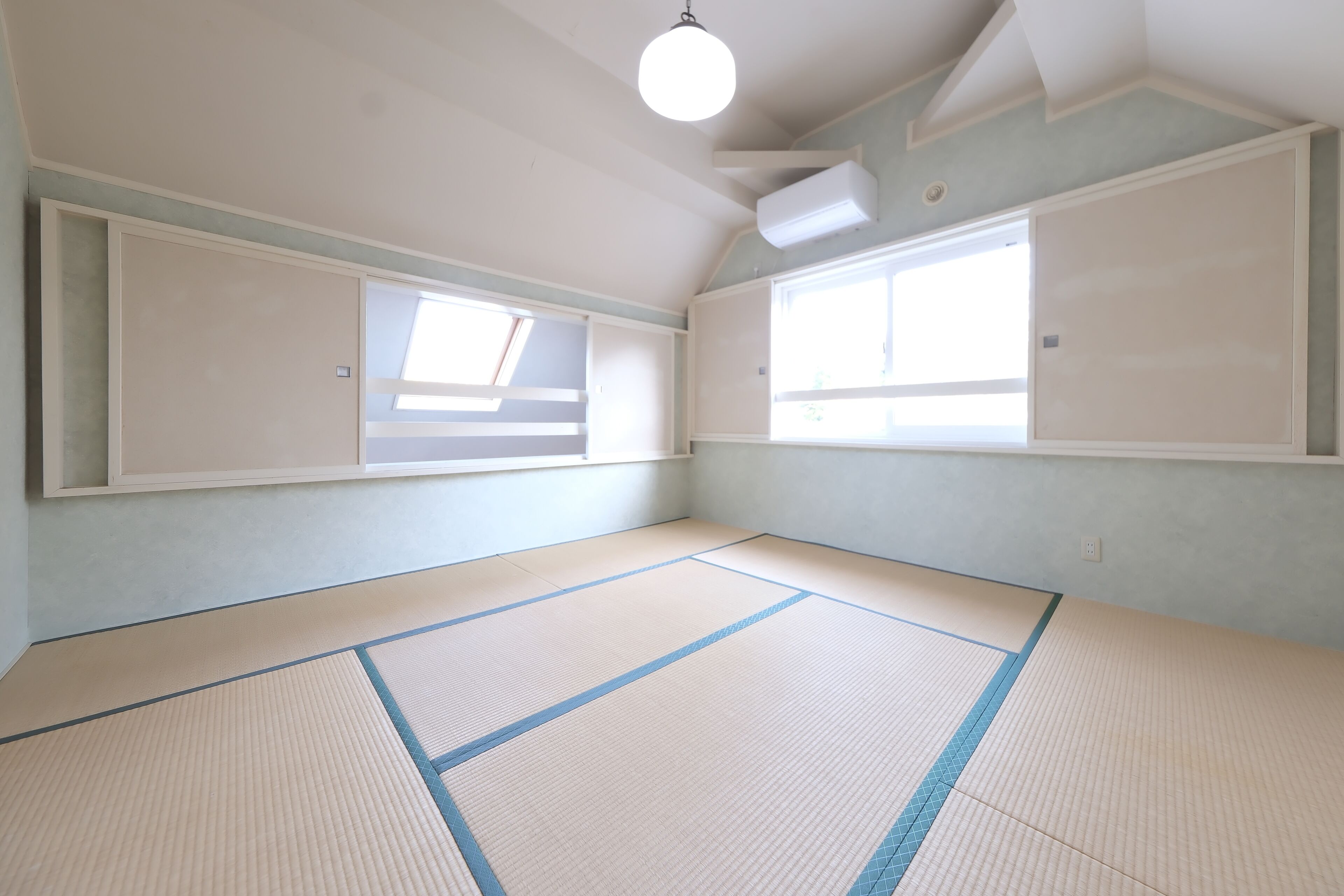 A room with tatami mats, two windows, and a ceiling fan.