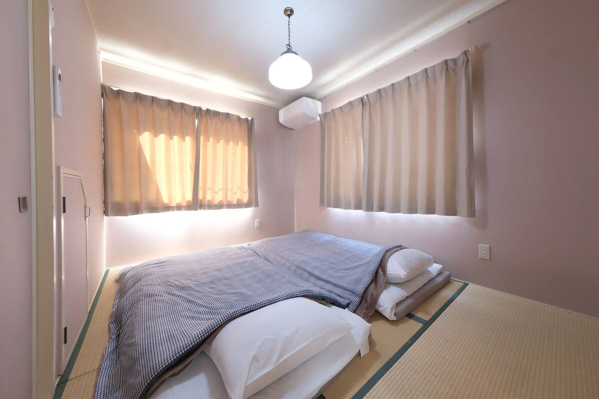 A bedroom with a bed, curtains, a ceiling light, and a wall socket.
