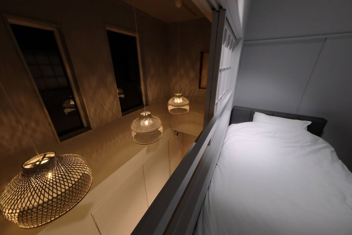 A modern hotel room with a bed, a hanging light fixture, and a window.
