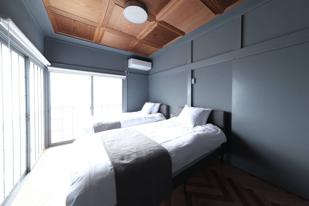 A bedroom with two beds, a wooden ceiling, and a large window.