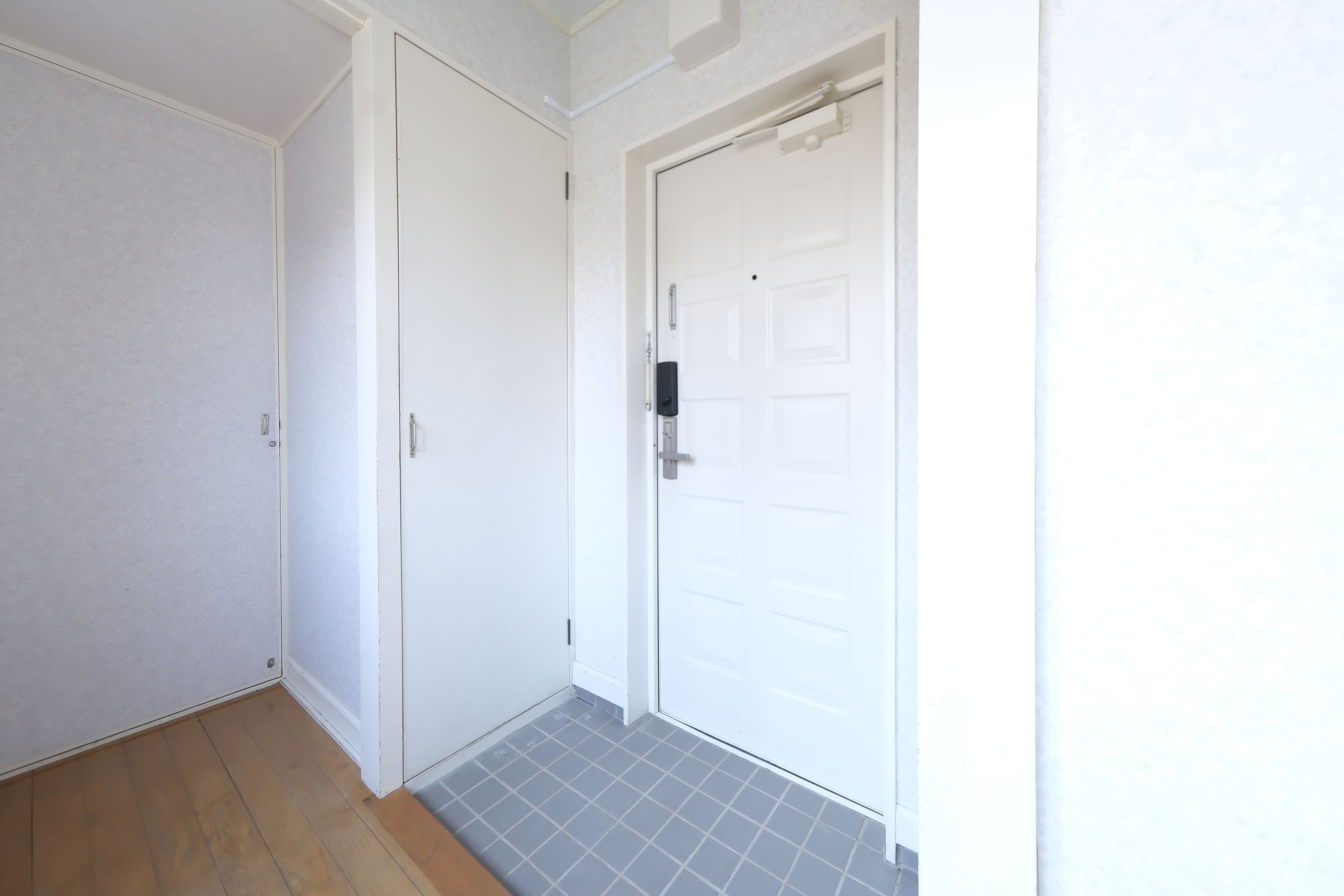 A hallway with a wooden floor, a white door with a black handle, and a white door with a silver handle.