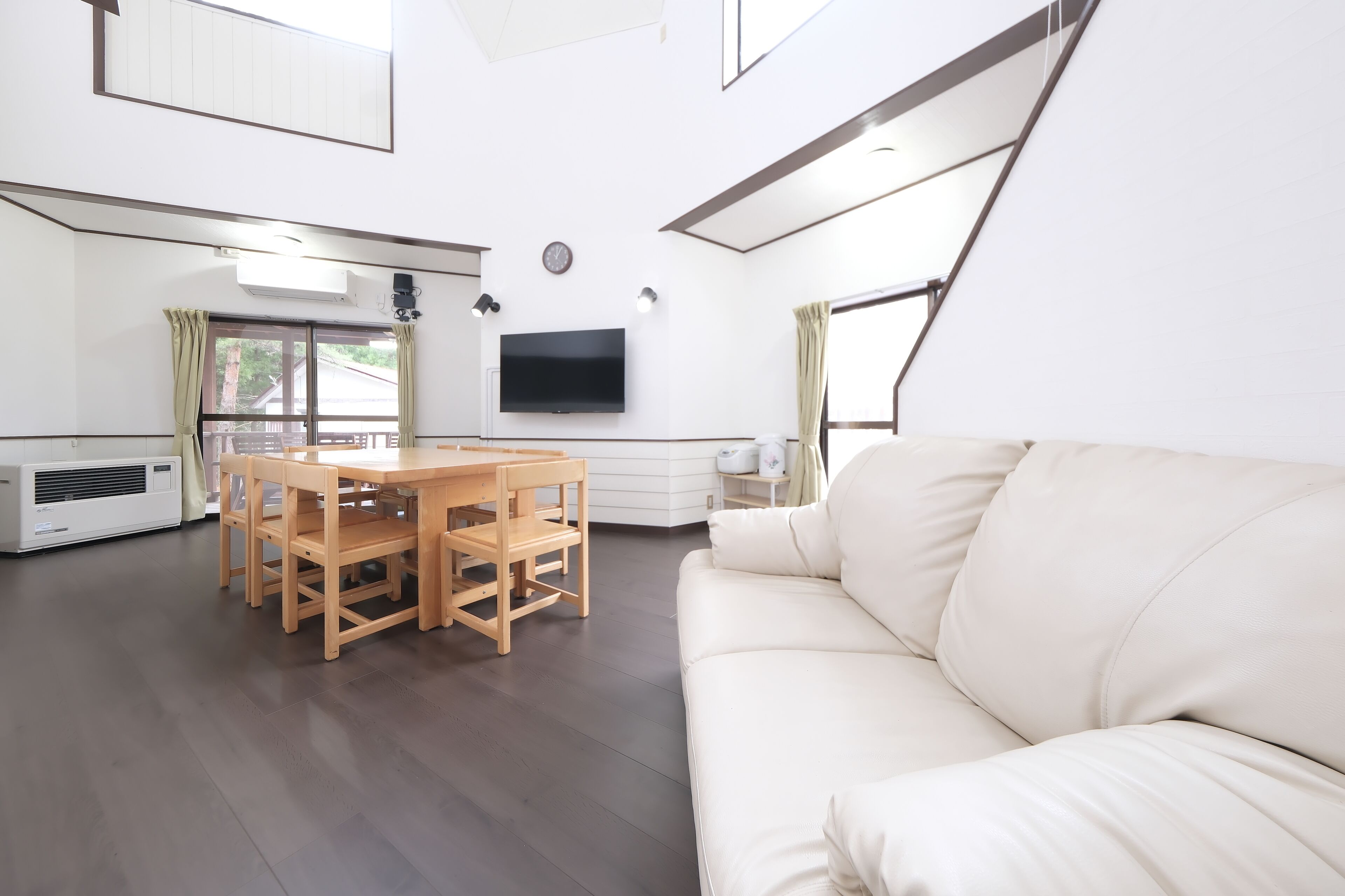 Una sala de estar moderna con un sofá, una mesa de comedor con sillas, un televisor de pantalla plana montado en la pared y un ventanal grande.