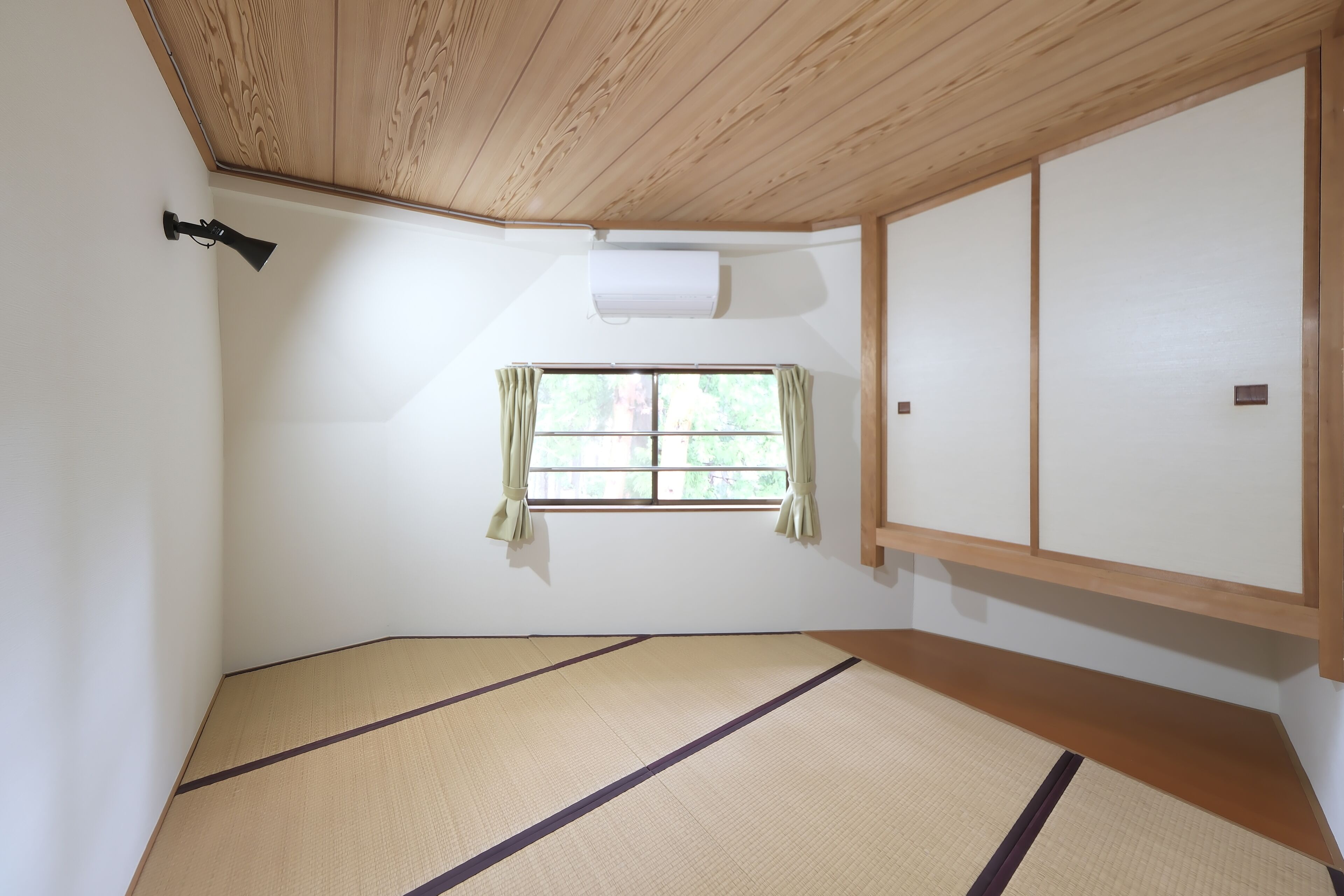 Una habitación con suelo de tatami, una ventana con cortinas, un ventilador de techo y una puerta corredera.