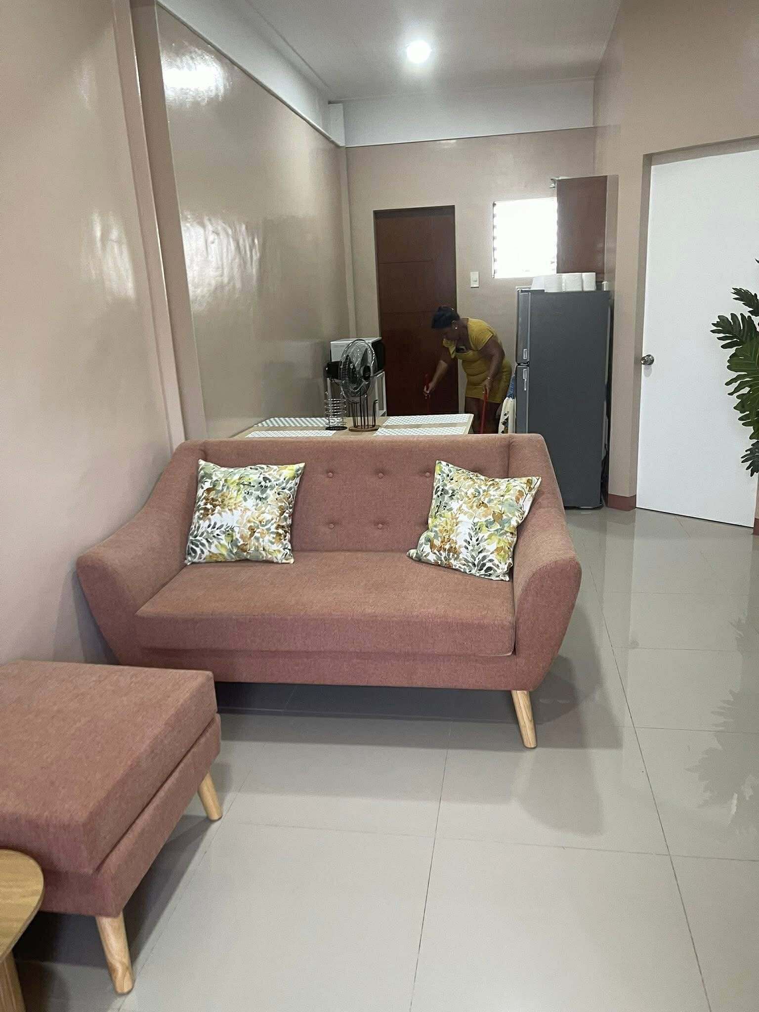A living room with a sofa, a small table, a refrigerator, and a door.