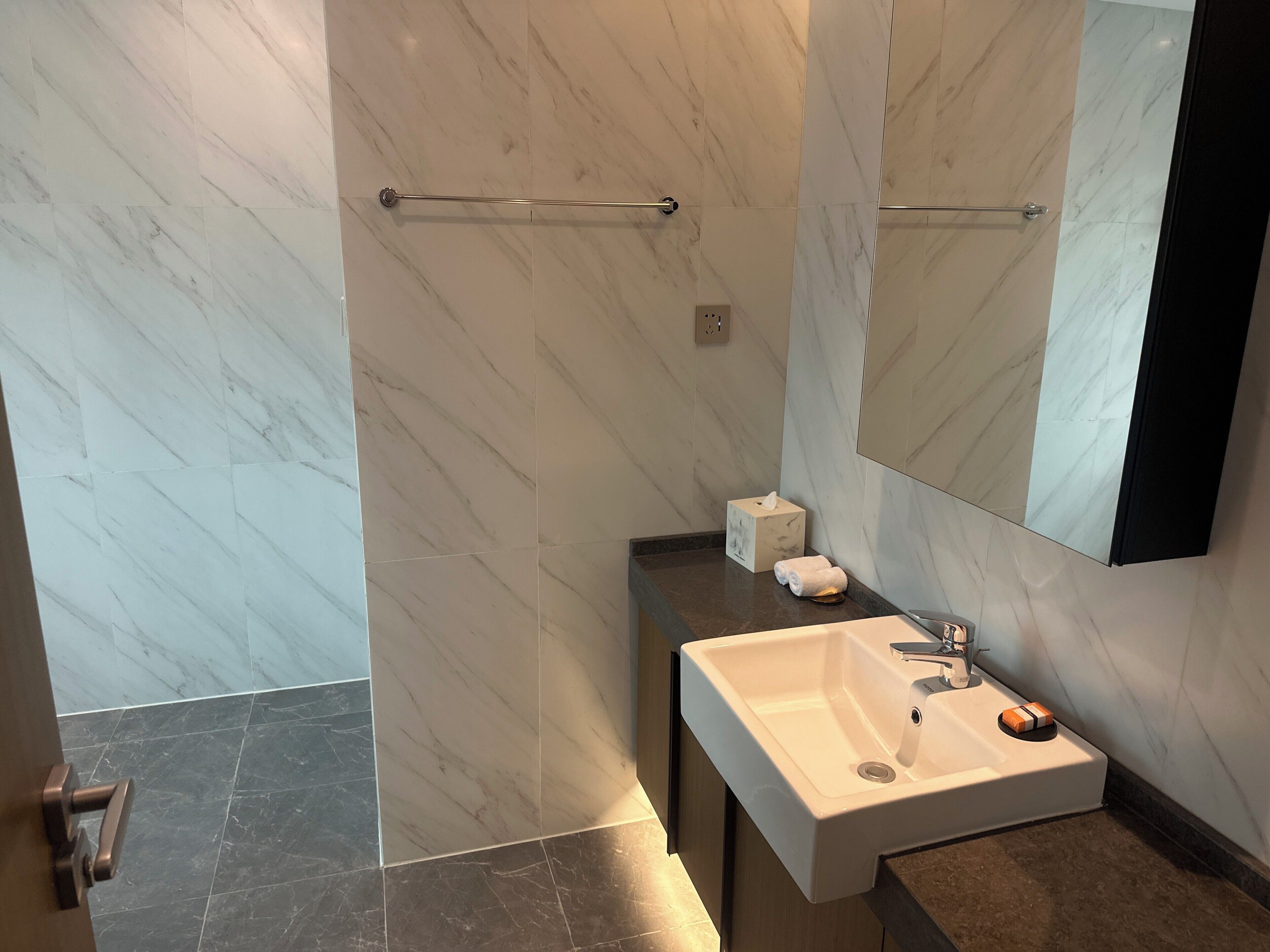 A modern bathroom with marble walls, a white sink, and a towel dispenser.