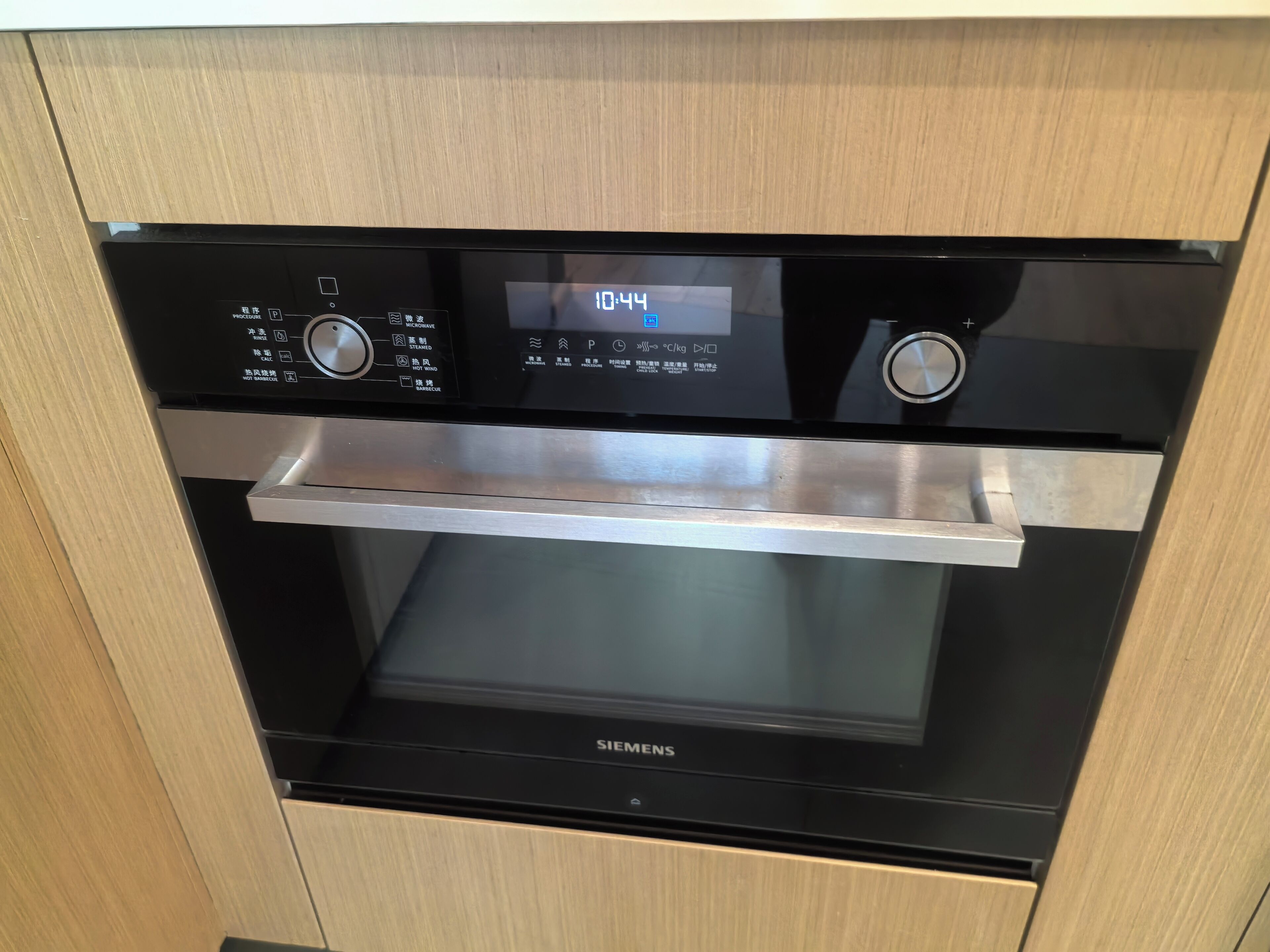 A Siemens oven with a digital clock displaying 10:44, a stainless steel shelf, and control knobs.