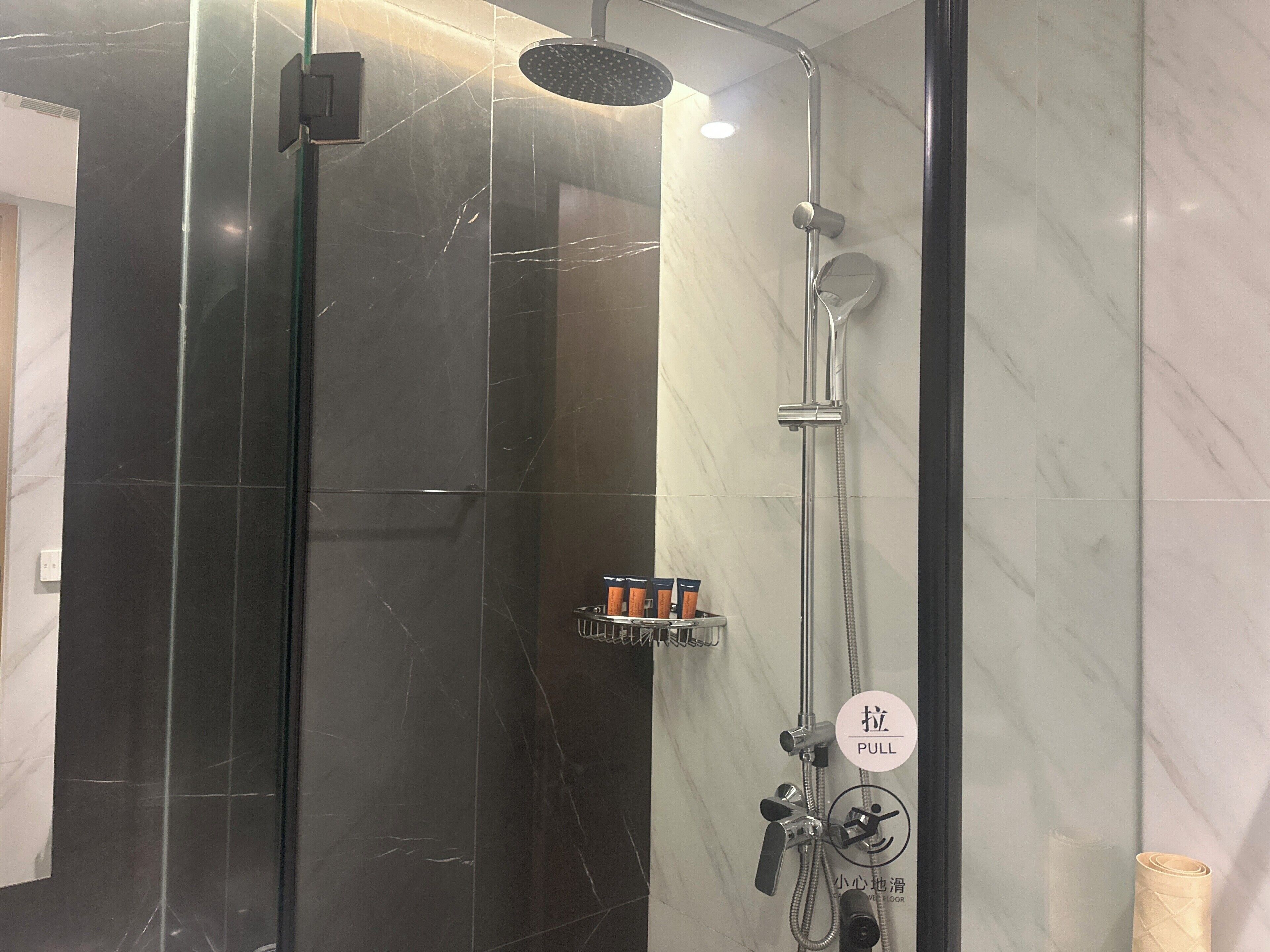 Une salle de bain moderne dotée d’une douche à parois de verre, d’un pommeau de douche à main, d’un robinet mural et d’un panneau de commande avec une poignée.