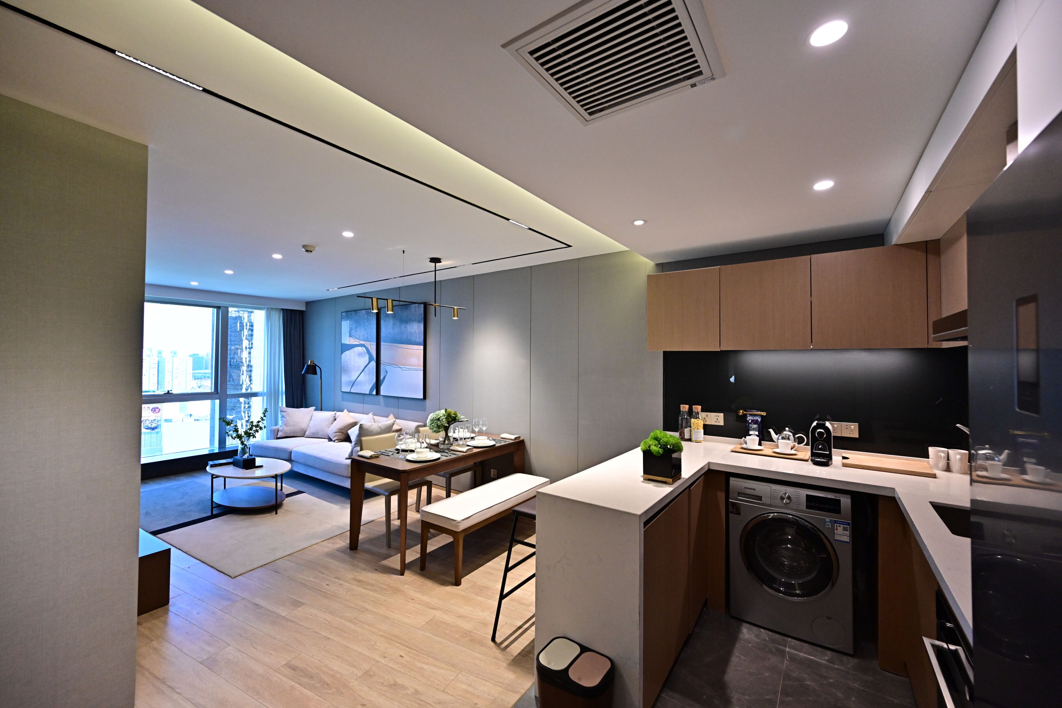 A modern kitchen with a built-in washer, a dining area with a sofa and table, and a large window providing natural light.