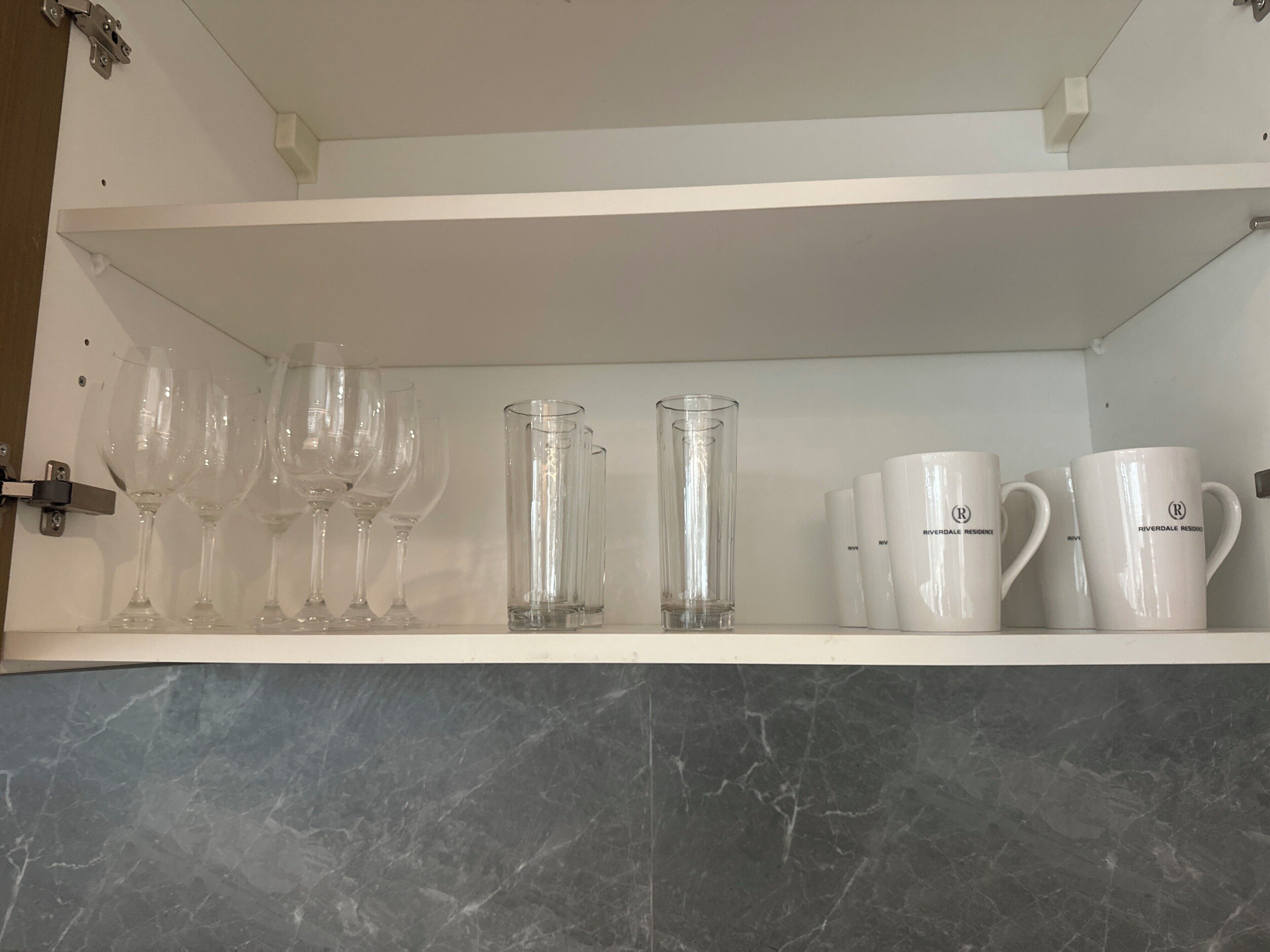A shelf with various glassware, including wine glasses and tumblers, and white mugs with a logo.