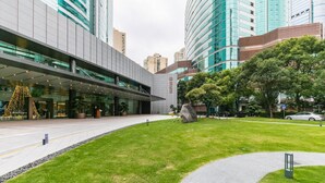 Un edificio moderno con fachada de vidrio, un área ajardinada con un camino y un árbol de Navidad.