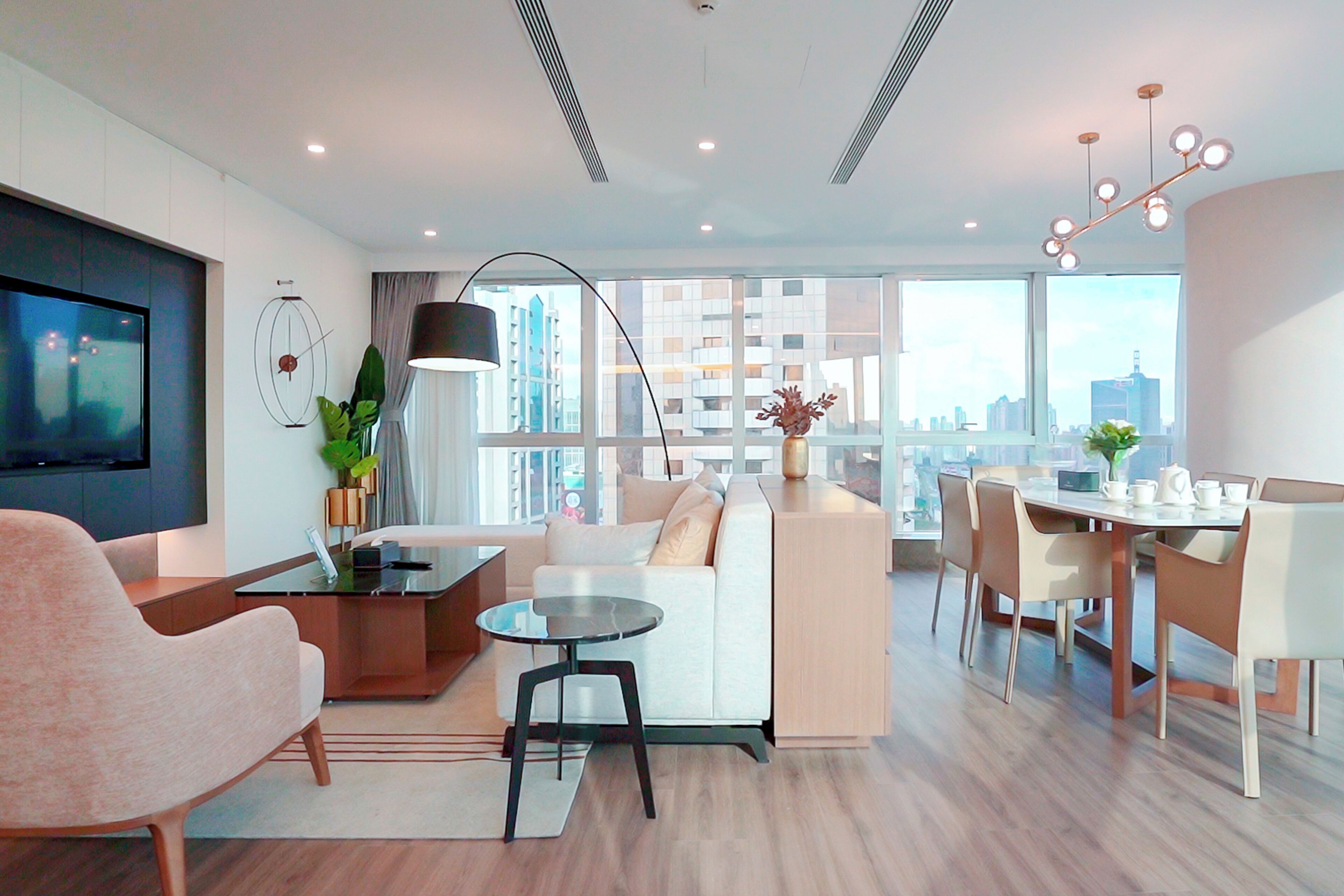 A modern living room with a sofa, a coffee table, a TV, and a dining area with chairs and a table.