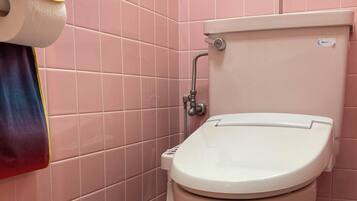 Un baño con paredes de azulejos rosados, un inodoro blanco y una toalla colgada en la pared.
