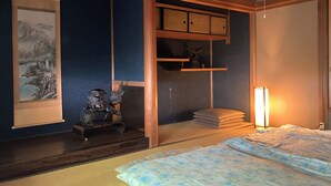 Una habitación tradicional japonesa con suelo de tatami, un fusuma, un pergamino colgado, una pequeña estatua y una lámpara de noche.