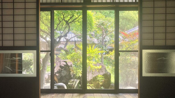Una habitación con puerta de vidrio corredera que da a un jardín con árboles y rocas.