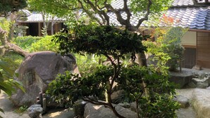 Un jardín japonés tradicional con formaciones rocosas, un árbol y un edificio con tejado de tejas.