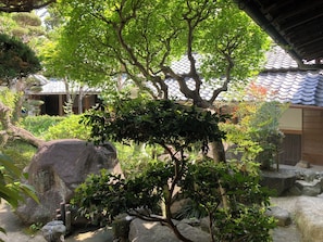 A traditional Japanese garden with rock formations, a tree, and a building with a tiled roof.