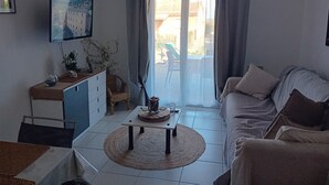 Uma sala de estar com sofá, mesa de centro, televisão na parede e vista pela janela.