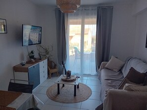 Ein Wohnzimmer mit Sofa, Couchtisch, Fernseher an der Wand und Blick durch das Fenster.
