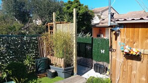 Um deck de madeira, um jardim cercado com várias plantas e um edifício com telhado de cerâmica.