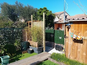 Eine Holzterrasse, ein eingezäunter Garten mit verschiedenen Pflanzen und ein Gebäude mit einem Ziegeldach.