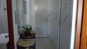 Um corredor com porta branca, espelho, uma mesa pequena com planta e parede com texto decorativo.