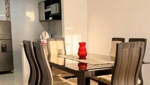 Un coin repas avec une table en verre, quatre chaises, un vase rouge et, au fond, une cuisine.