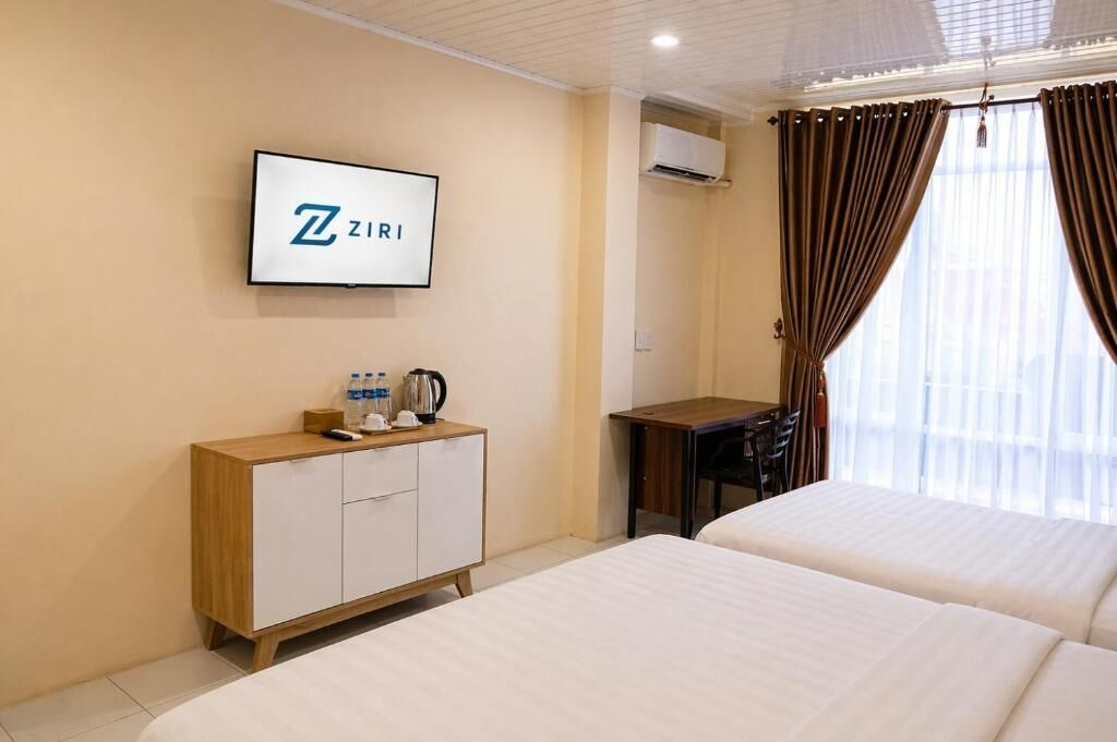 Quarto de hotel com duas camas, uma TV fixada na parede, um armário de madeira com uma chaleira e uma escrivaninha.