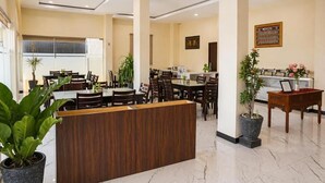 En hotellobby med flera matbord, en receptionsdisk och krukväxter.