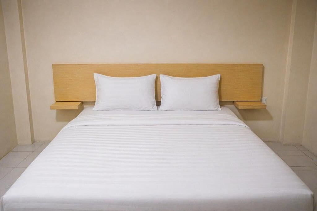 A bed with a wooden headboard and two pillows, a bedside table, and a plain wall.