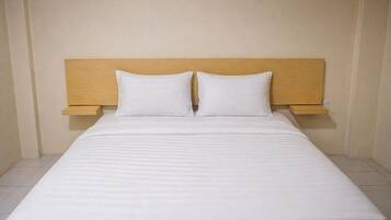 A bed with a wooden headboard and two pillows, a bedside table, and a plain wall.