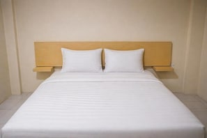 A bed with a wooden headboard and two pillows, a bedside table, and a plain wall.