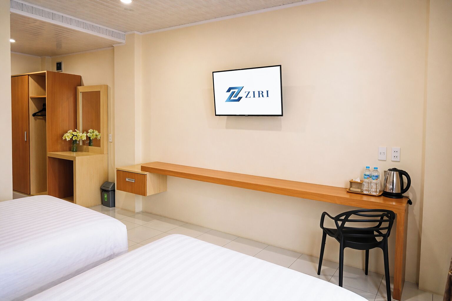 Ein Hotelzimmer mit zwei Betten, einem Schreibtisch mit Stuhl, einem Kleiderschrank und einem ZIRI-Schild an der Wand.