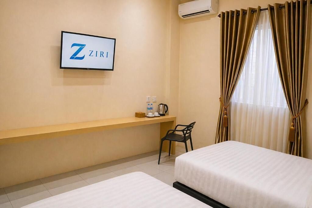 Quarto de hotel com duas camas, uma mesa com cadeira, uma cafeteira e um letreiro ZIRI na parede.