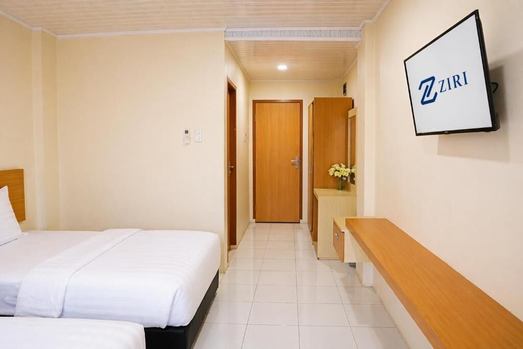 A hotel room with two beds, a TV mounted on the wall, and a wooden bench.