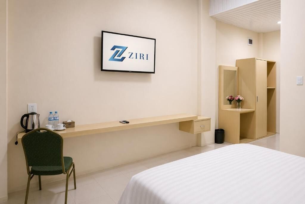 Habitación de hotel con cama, escritorio y silla, armario, un logo enmarcado en la pared y un cubo de basura.