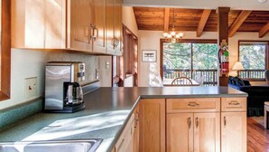 A kitchen with wooden cabinets, a stainless steel refrigerator, and a dining area with a view of trees. - 3 Bedroom Cabin in the Woods located in Yosemite Park (Yosemite National Park)