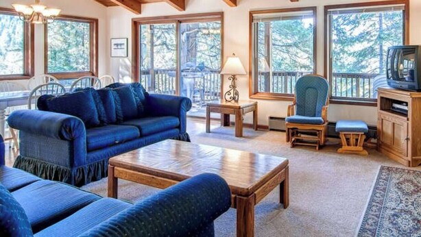 A cozy living room with a wooden ceiling, large windows, a blue sofa, a coffee table, and a television. - 3 Bedroom Cabin in the Woods located in Yosemite Park (Yosemite National Park)