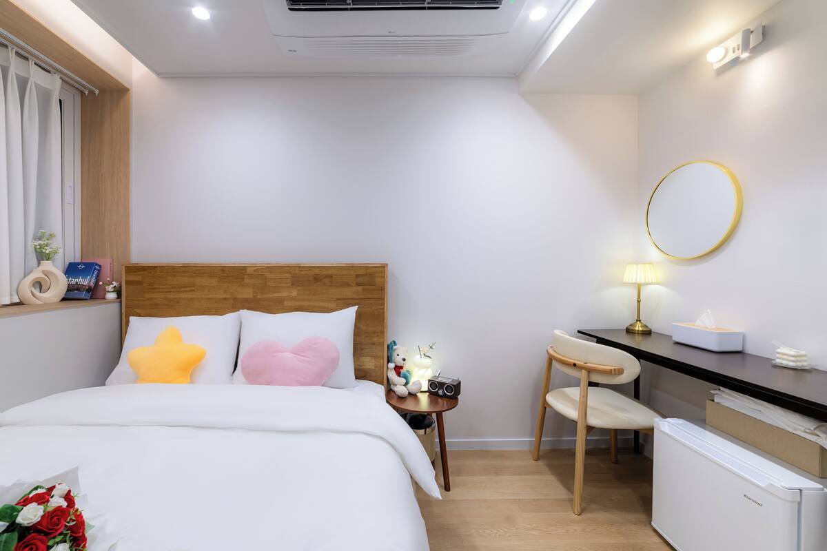 A hotel room with a bed, bedside table, desk, chair, and a small refrigerator.