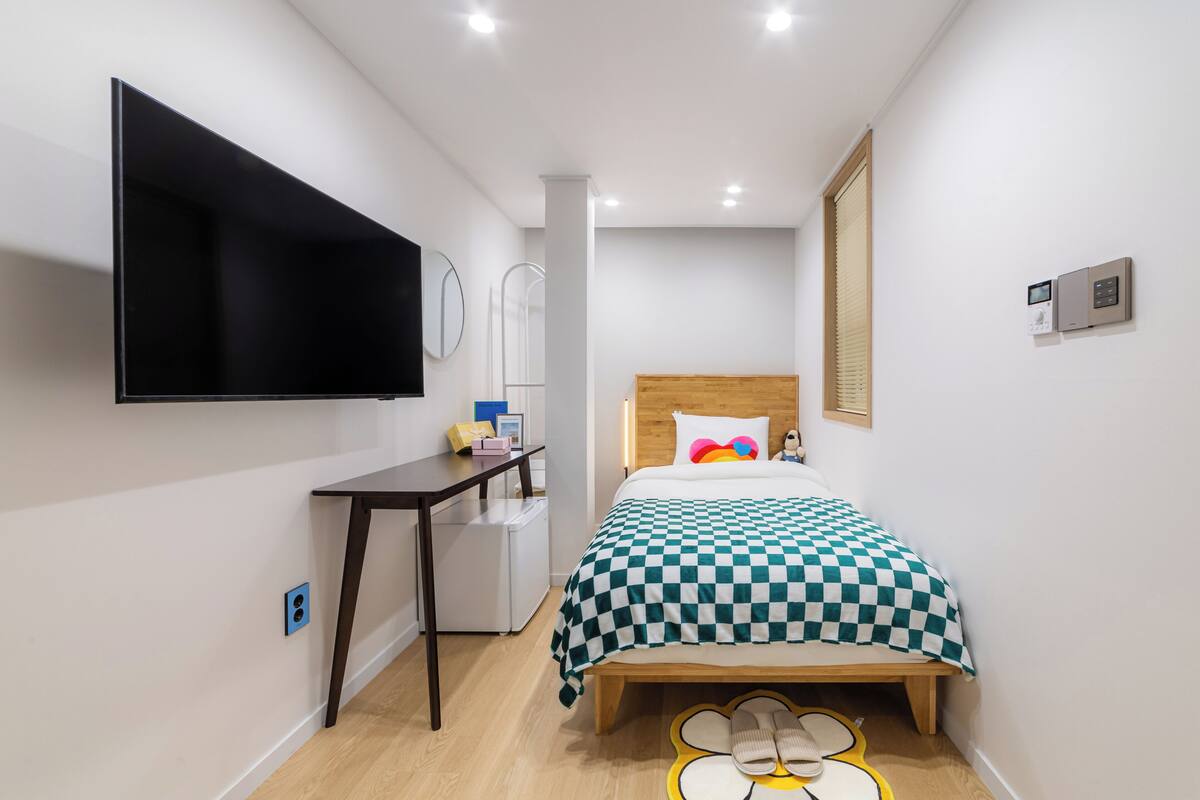 A hotel room with a bed, a desk, a TV, and a small refrigerator.