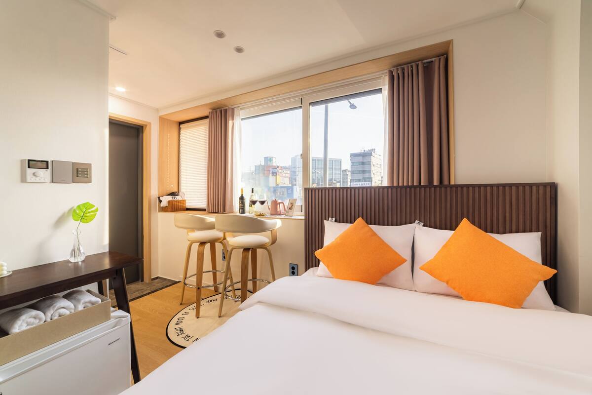 A hotel room with a bed, a desk, a chair, a small refrigerator, and a window with curtains.