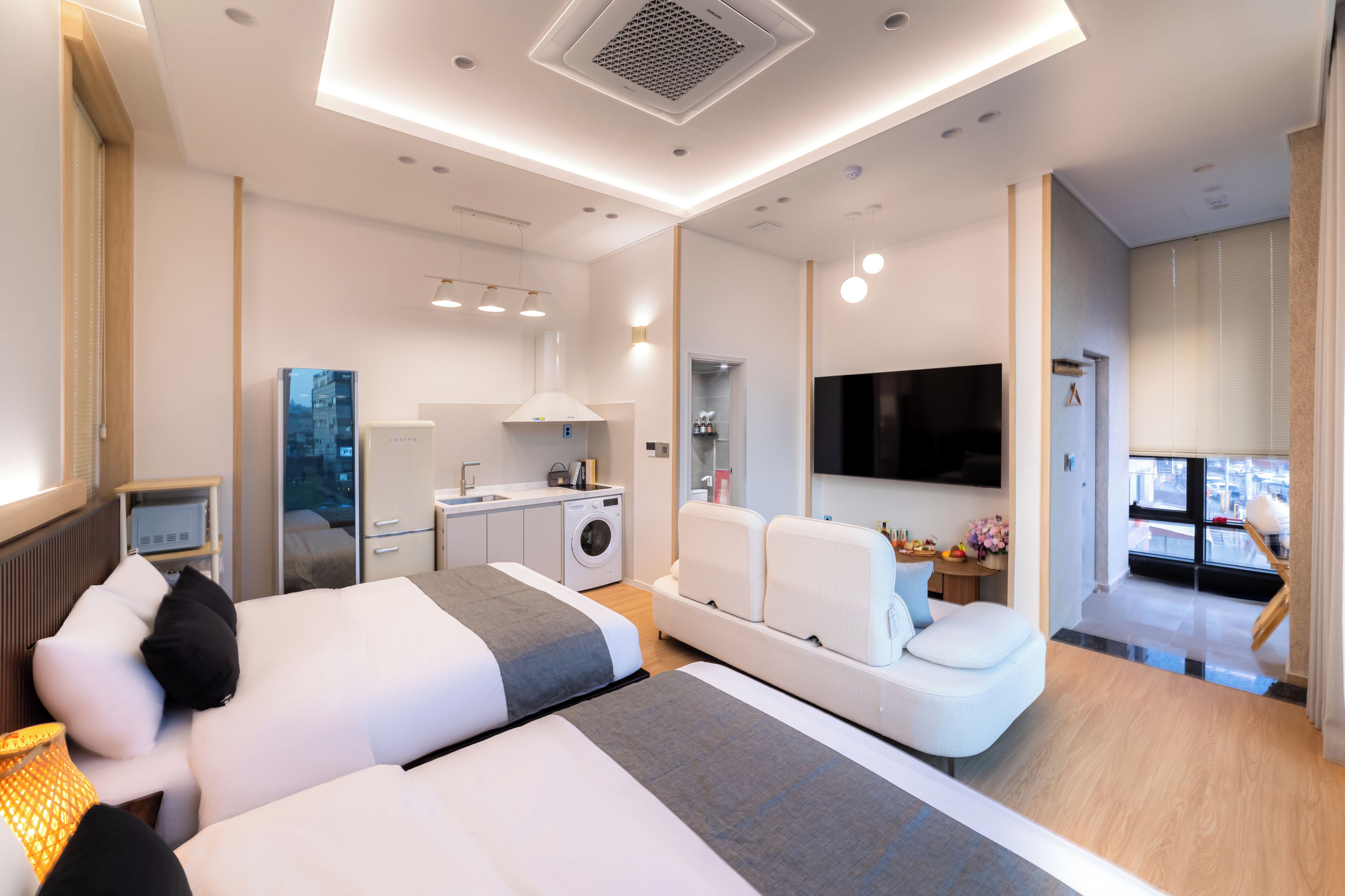 Una habitación de hotel moderna con una cama grande, un sofá, un televisor, una lavadora y una kitchenette.