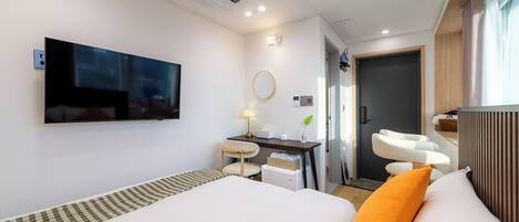 A modern hotel room with a bed, a desk, a chair, a TV, a mirror, and a bathroom.