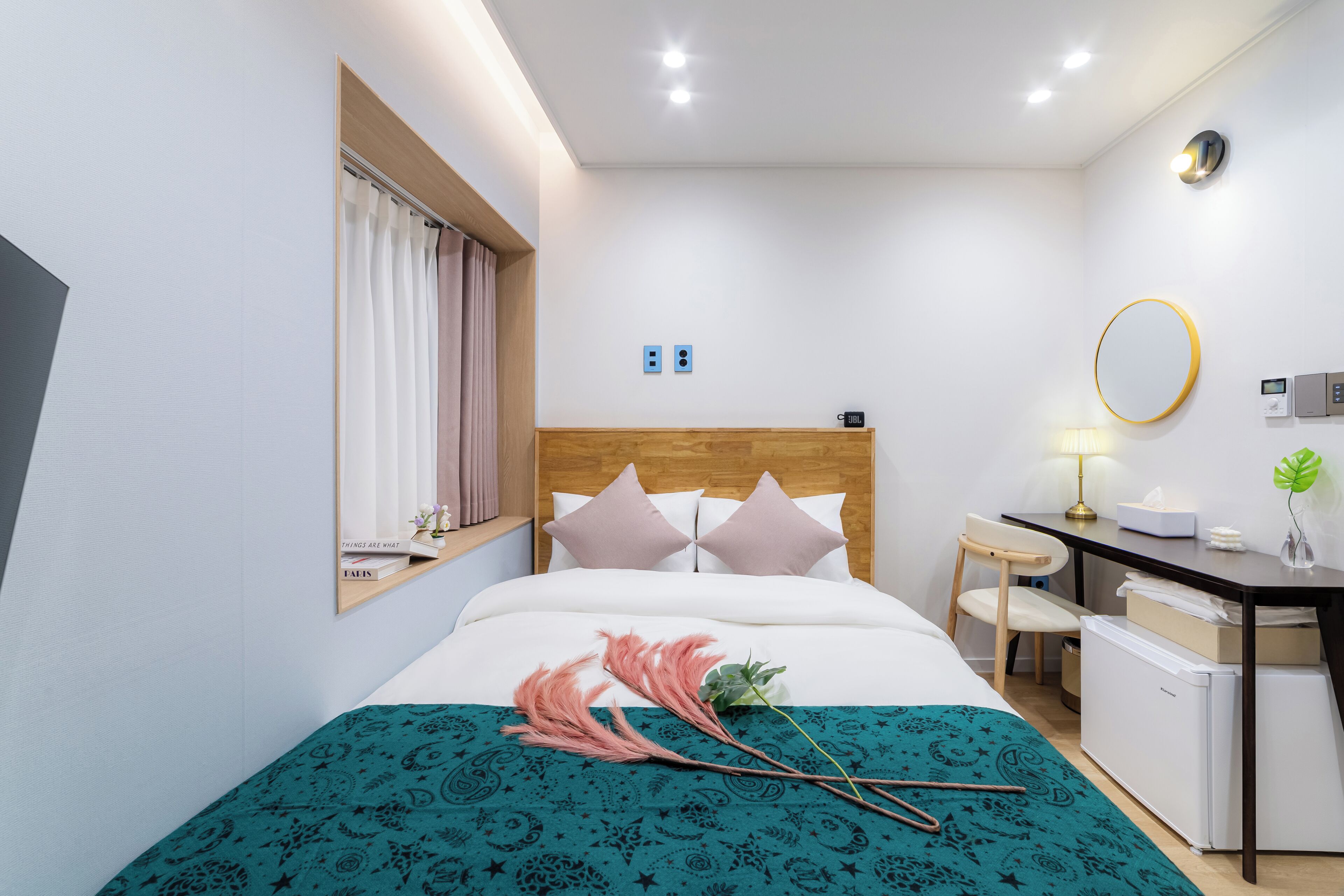 A hotel room with a bed, a desk, a chair, a small refrigerator, and a window with curtains.