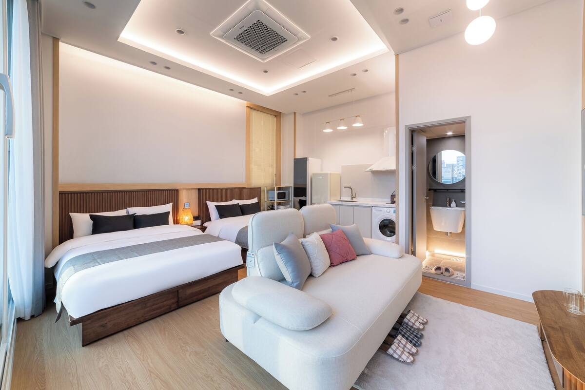 A modern hotel room with a large bed, a sofa, a washing machine, and a bathroom.