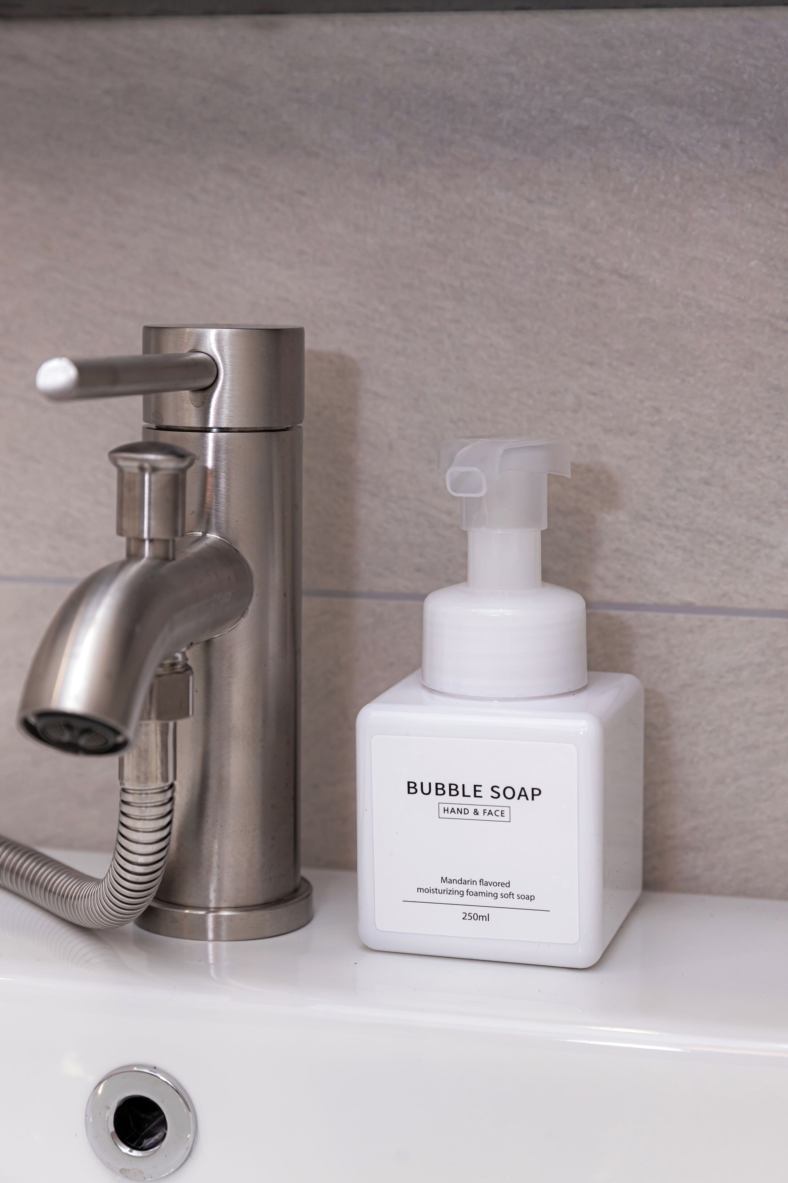 A bathroom with a modern faucet and a bottle of bubble soap.