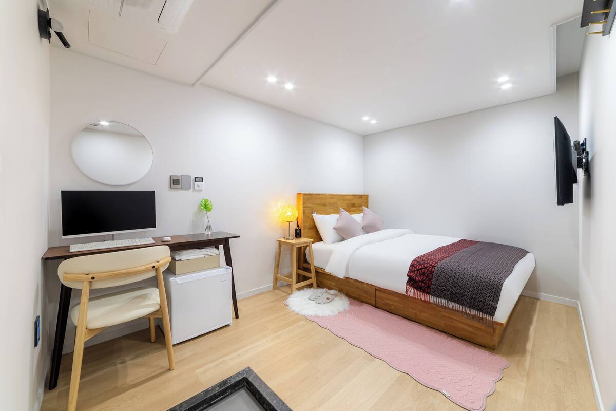 A modern bedroom with a bed, desk, chair, and a small refrigerator.