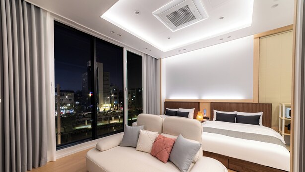Una habitación de hotel moderna con una cama grande, un sofá, vista a la ciudad y un tragaluz.